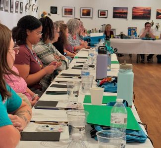 Students sit around a table for a group art class.